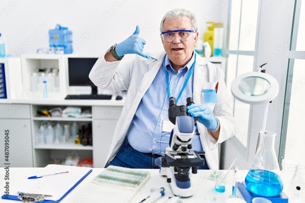Senior caucasian man working at scientist laboratory smiling doing phone gesture with hand and fingers like talking on the telephone. communicating concepts. Senior caucasian man working at scientist laboratory smiling doing phone gesture with hand and fingers like talking on the telephone. communicating concepts.