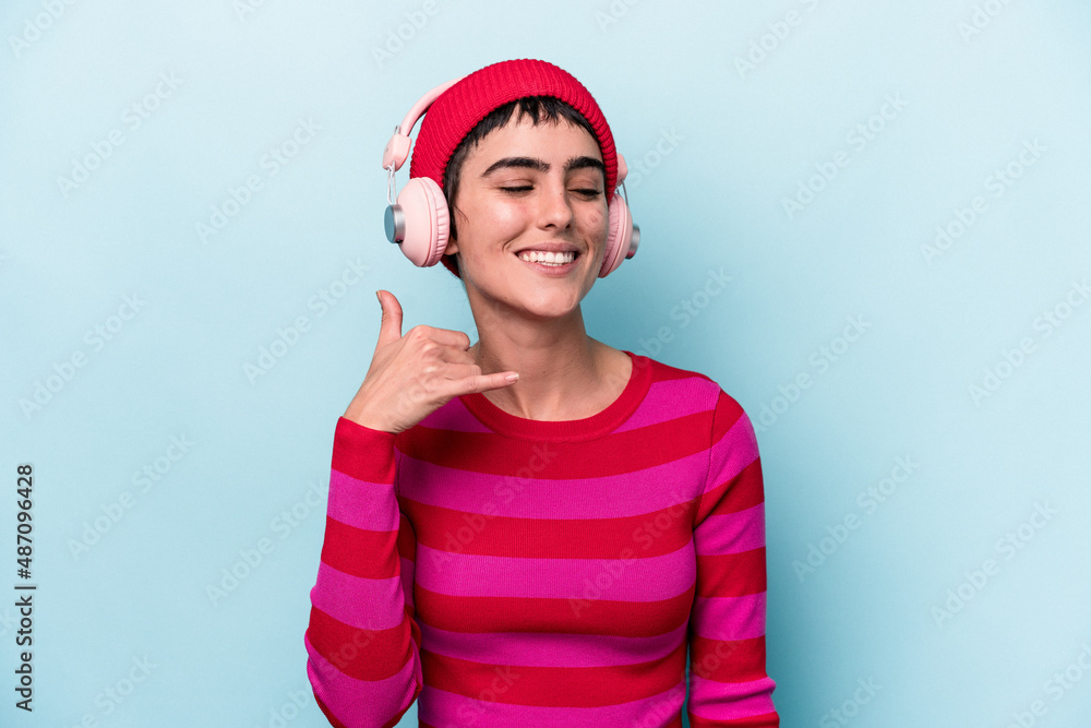 Young caucasian woman listening to music isolated on background showing a mobile phone call gesture with fingers.