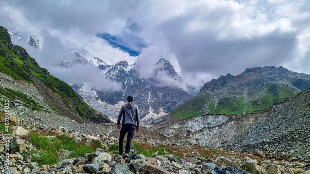 A man hiking and enjoying the panoramic view on the Shkhara Glacier in the Greater Caucasus Mountain Range in Georgia, Svaneti Region, Ushguli. Wanderlust, Alpine pasture. Freedom