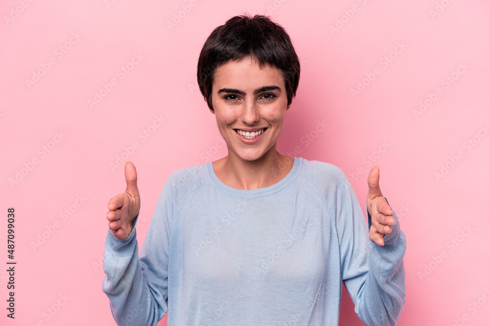 Young caucasian woman isolated on pink background holding something with both hands, product presentation. Young caucasian woman isolated on pink background holding something with both hands, product presentation.