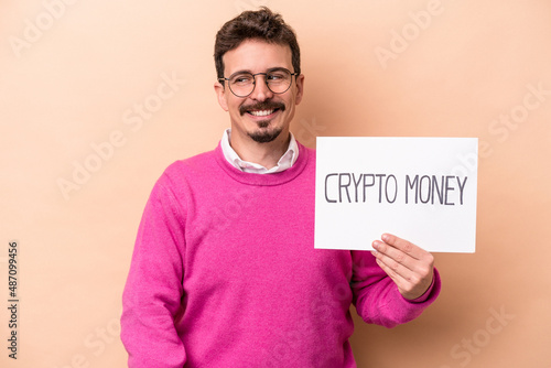 Young caucasian man holding a crypto money placard isolated on beige background looks aside smiling, cheerful and pleasant.