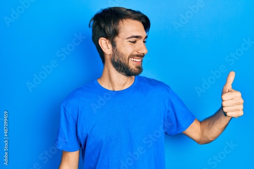 Young hispanic man wearing casual clothes looking proud, smiling doing thumbs up gesture to the side