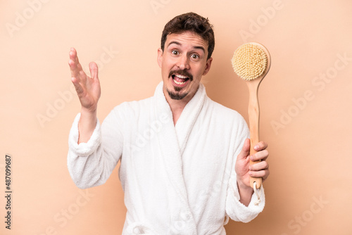Young caucasian man holding back scratcher isolated on beige background receiving a pleasant surprise, excited and raising hands.