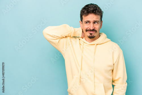 Young caucasian man isolated on blue background touching back of head, thinking and making a choice.
