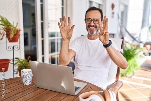 Middle age man using computer laptop at home showing and pointing up with fingers number eight while smiling confident and happy.
