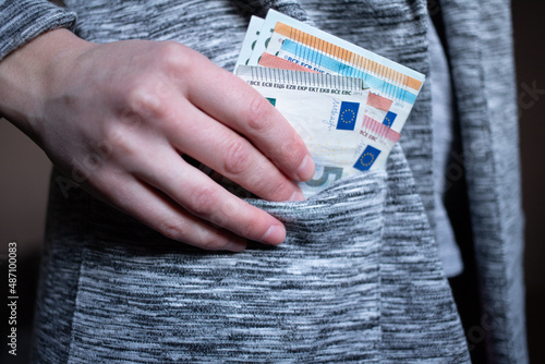 Woman's hand puts or takes out paper money 5 euro into the pocket of a gray jacket, cardigan photo