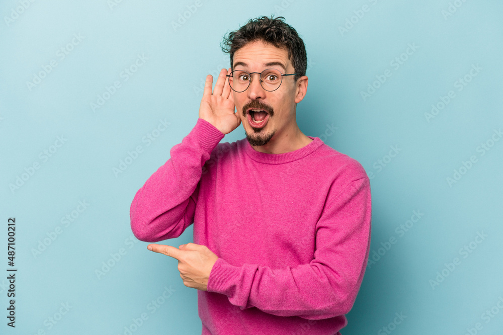 Young caucasian man isolated on blue background trying to listening a gossip. Young caucasian man isolated on blue background trying to listening a gossip.