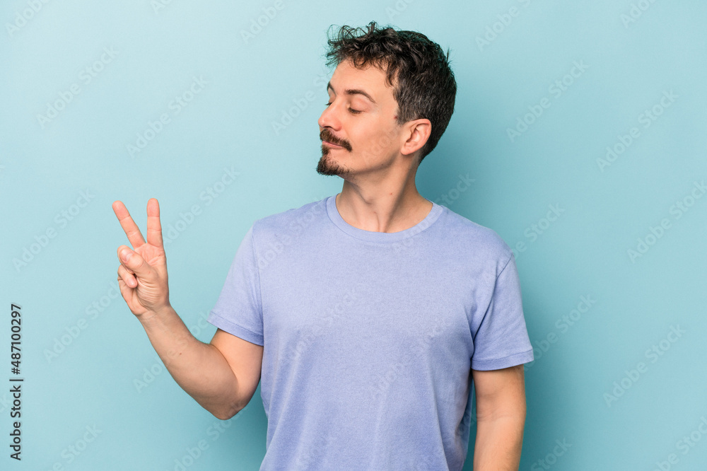 Fototapeta premium Young caucasian man isolated on blue background joyful and carefree showing a peace symbol with fingers.