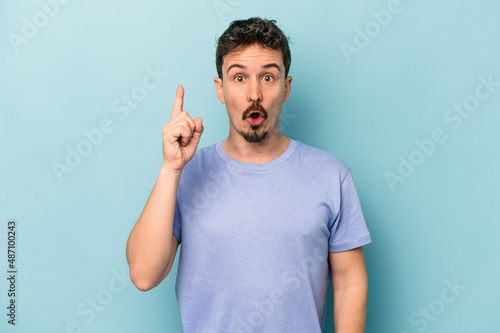Young caucasian man isolated on blue background pointing upside with opened mouth. © Asier