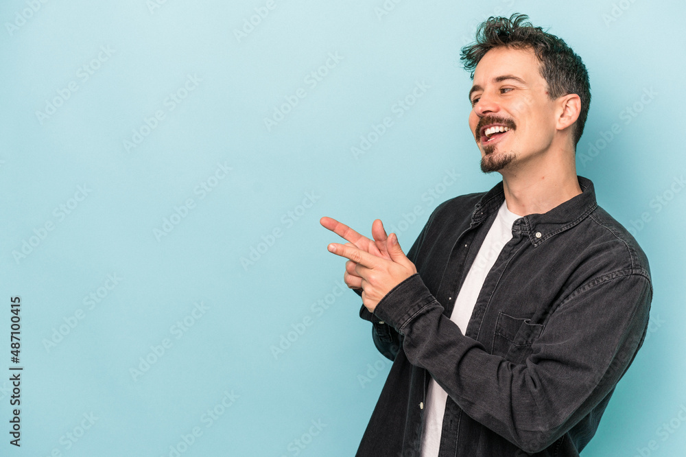 Young caucasian man isolated on blue background points with thumb finger away, laughing and carefree. Young caucasian man isolated on blue background points with thumb finger away, laughing and carefree.
