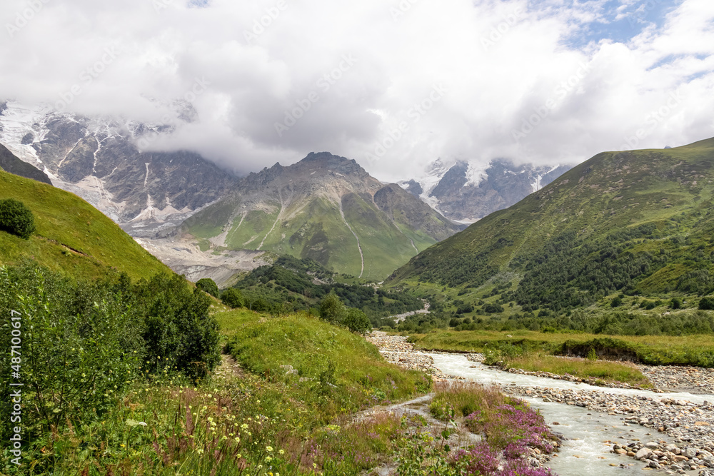 Patara Enguri River flowing down the a valley in the Greater Caucasus Mountain Range in Georgia, Svaneti Region, Ushguli. The Shkhara Mountain is covered by clouds. Snow-capped mountains.Glacier