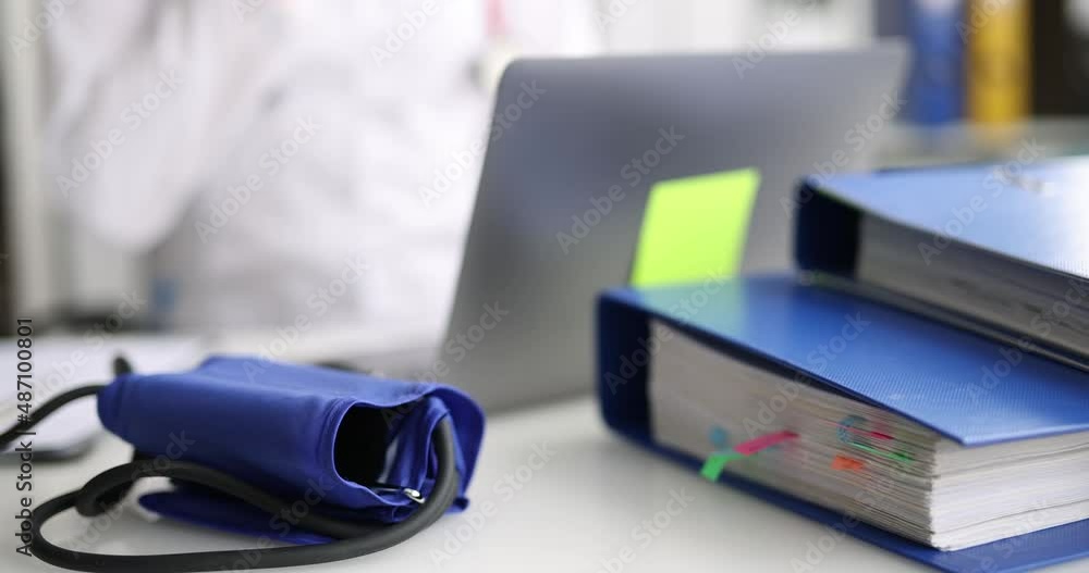 Tonometer and folders with documents lying at workplace of doctor with laptop closeup 4k movie