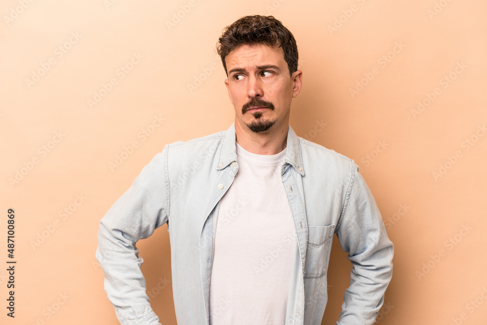 Young caucasian man isolated on beige background confused, feels doubtful and unsure. Young caucasian man isolated on beige background confused, feels doubtful and unsure.