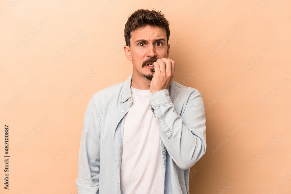 Young caucasian man isolated on beige background biting fingernails, nervous and very anxious. Young caucasian man isolated on beige background biting fingernails, nervous and very anxious.