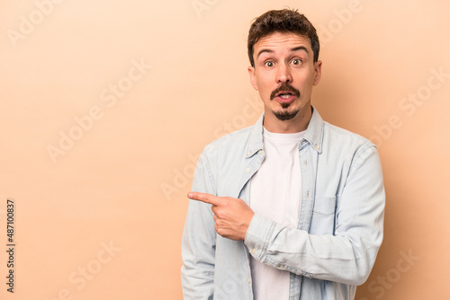 Young caucasian man isolated on beige background pointing to the side © Asier