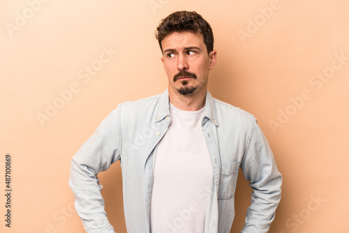 Young caucasian man isolated on beige background confused, feels doubtful and unsure.