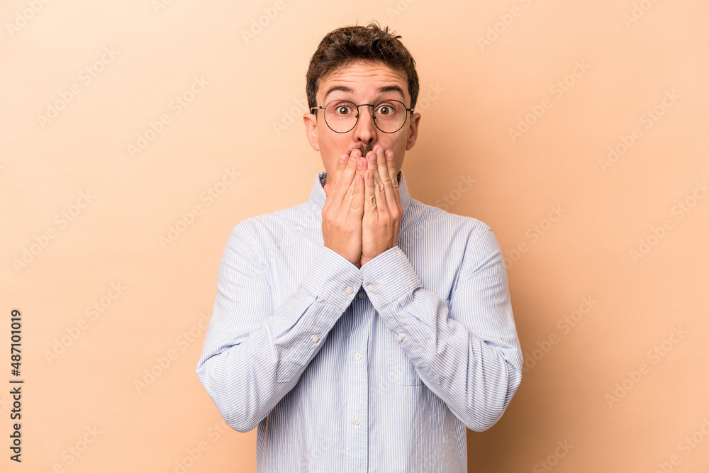 Young caucasian man isolated on beige background shocked, covering mouth with hands, anxious to discover something new. Young caucasian man isolated on beige background shocked, covering mouth with hands, anxious to discover something new.