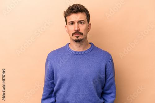 Young caucasian man isolated on beige background sad, serious face, feeling miserable and displeased.