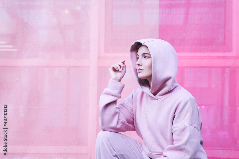 A young woman on an isolated pink background. She sits with one hand on her knee and looks away with a thoughtful face. High quality photo A young woman on an isolated pink background. She sits with one hand on her knee and looks away with a thoughtful face. High quality photo