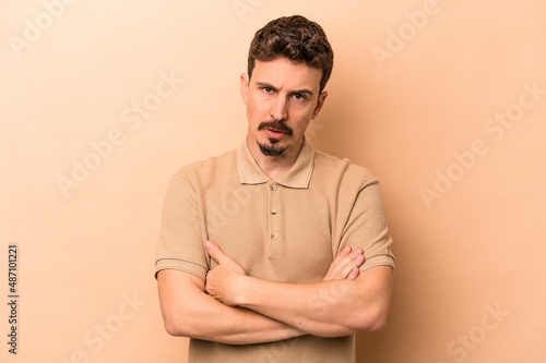 Young caucasian man isolated on beige background who is bored, fatigued and need a relax day.