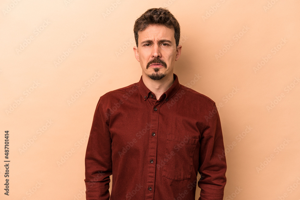 Obraz premium Young caucasian man isolated on beige background sad, serious face, feeling miserable and displeased.