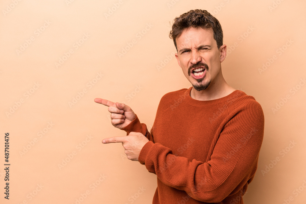 Young caucasian man isolated on beige background pointing with forefingers to a copy space, expressing excitement and desire. Young caucasian man isolated on beige background pointing with forefingers to a copy space, expressing excitement and desire.