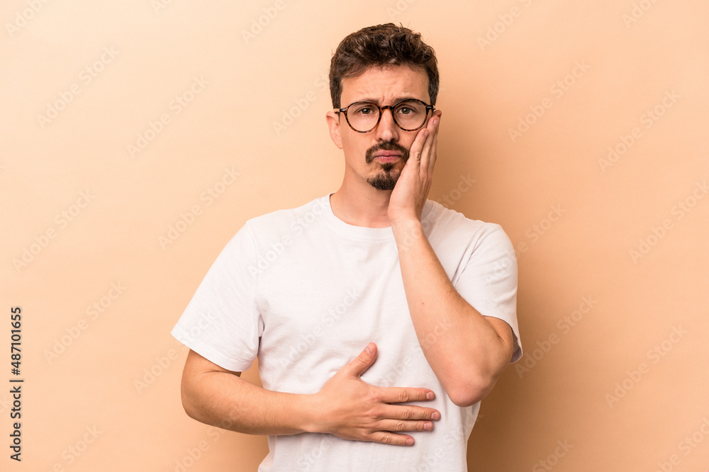 Young caucasian man isolated on beige background blows cheeks, has tired expression. Facial expression concept. Young caucasian man isolated on beige background blows cheeks, has tired expression. Facial expression concept.