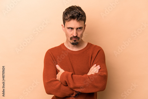Young caucasian man isolated on beige background tired of a repetitive task.