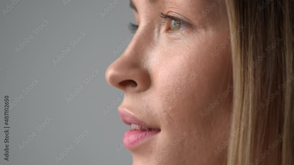 Beauty face of a young blonde woman in profile close-up. Smile, beautiful eyes, lips and teeth. Grey background