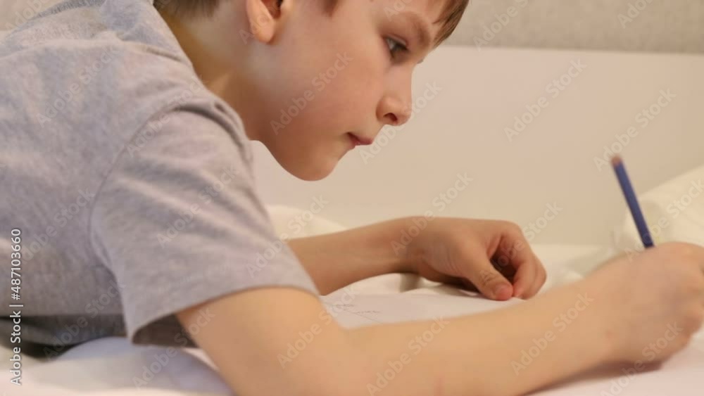a seven-year-old boy passionately drawing with a simple pencil lying on the couch. portrait close-up side view a seven-year-old boy passionately drawing with a simple pencil lying on the couch. portrait close-up side view
