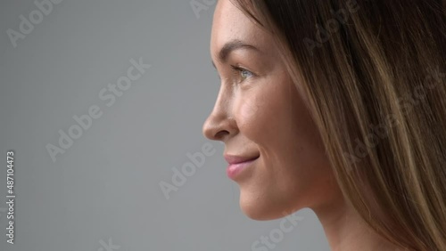 Beauty face of a young blonde woman in profile close-up. Smile, beautiful eyes, lips and teeth. Grey background