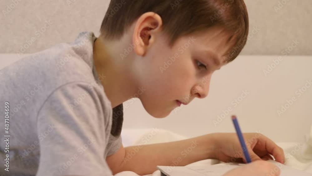 a seven-year-old boy passionately drawing with a simple pencil lying on the couch. portrait close-up side view a seven-year-old boy passionately drawing with a simple pencil lying on the couch. portrait close-up side view