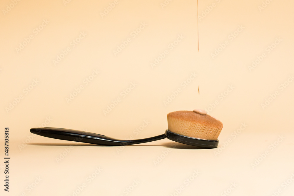 Brush for applying foundation on the face on a nude background. Foundation, cosmetics flowing on the brush, personal care, makeup - obrazy, fototapety, plakaty 