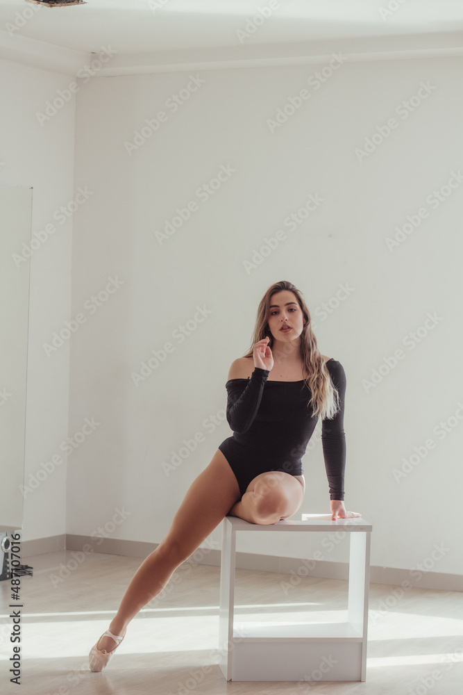A woman sitting on the table, in a dance studio, dressed in a dance outfit, looking into the camera. A woman sitting on the table, in a dance studio, dressed in a dance outfit, looking into the camera.