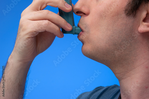 Asthma inhaler, generic, non-branded, being used by unrecognizable by man. Close up studio shot, isolated on blue background
