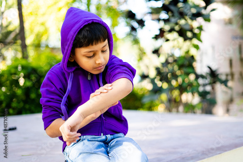 young indian kid itching skin or rashes at park - concept of skincare, allergy, winter infecton and medical photo