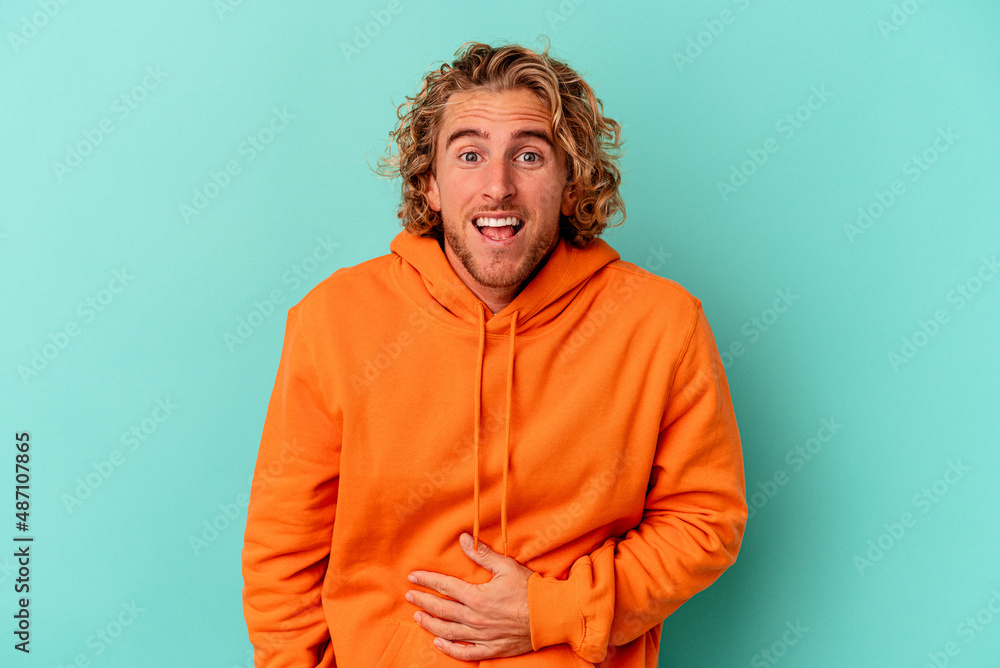 Young caucasian man isolated on blue background touches tummy, smiles gently, eating and satisfaction concept.