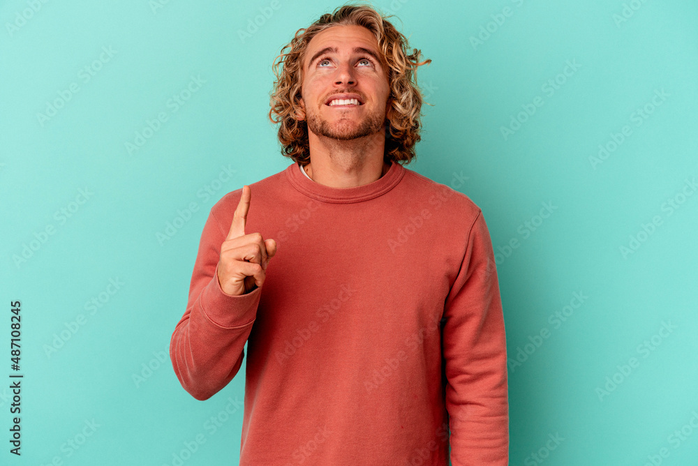 Young caucasian man isolated on blue background indicates with both fore fingers up showing a blank space. Young caucasian man isolated on blue background indicates with both fore fingers up showing a blank space.