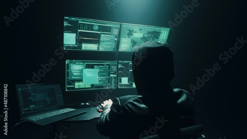 Concept shot of anonymous man hacker using computer to hack private data worldwide while sitting at desk in obscure room photo