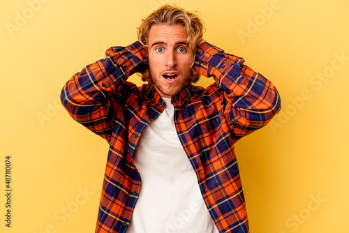 Young caucasian man isolated on yellow background covering ears with hands trying not to hear too loud sound.