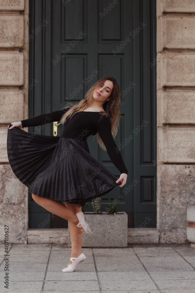 A woman going into a dance pose in front of a building,   dressed in a dance outfit.