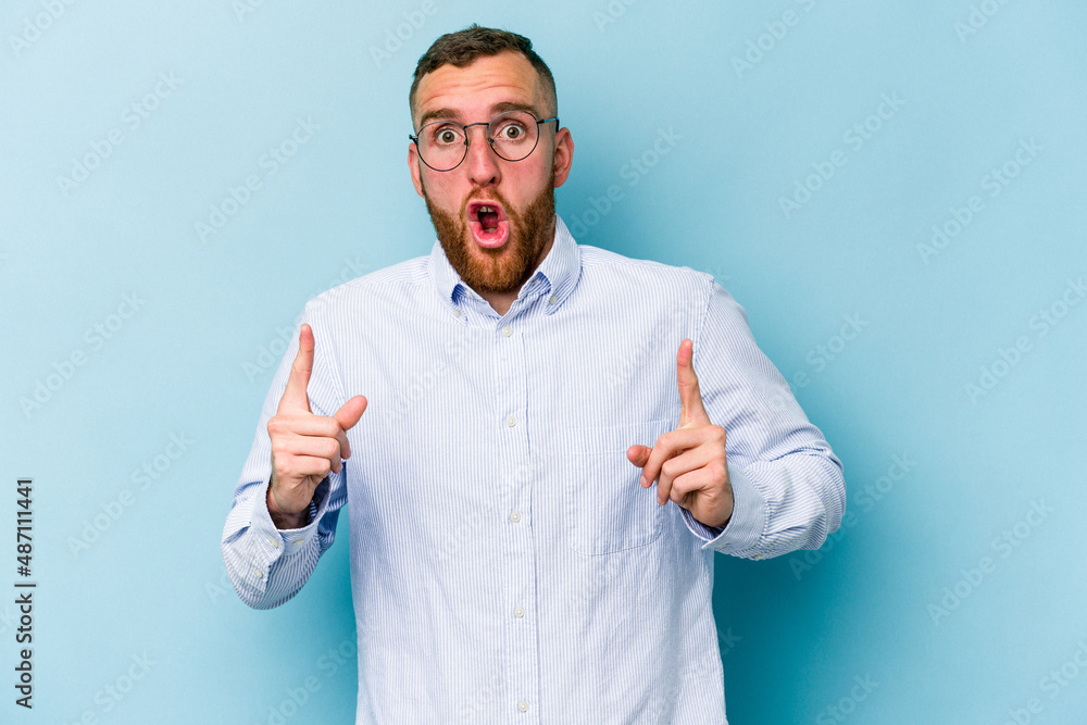 Young caucasian man isolated on blue background pointing upside with opened mouth. Young caucasian man isolated on blue background pointing upside with opened mouth.