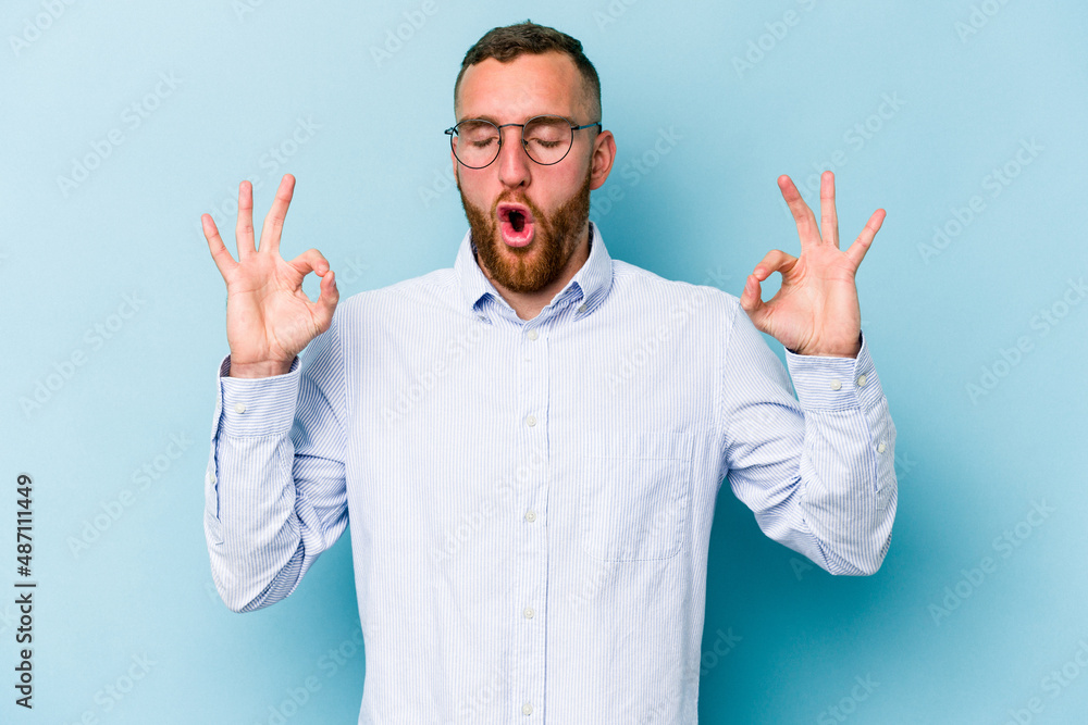 Young caucasian man isolated on blue background relaxes after hard working day, she is performing yoga. Young caucasian man isolated on blue background relaxes after hard working day, she is performing yoga.