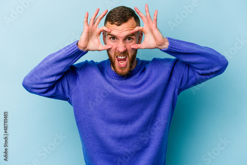 Young caucasian man isolated on blue background keeping eyes opened to find a success opportunity.