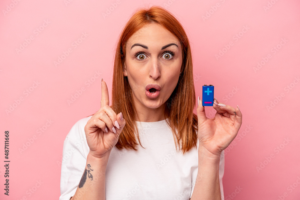 Young caucasian woman holding a batteries isolated on pink background having some great idea, concept of creativity. Young caucasian woman holding a batteries isolated on pink background having some great idea, concept of creativity.