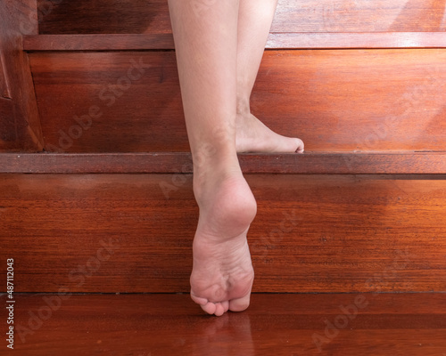 Barefoot legs of a female on iron wooden (in Indonesia called Merbau wooden with natural varnished wood texture) stairs, at residential home. 
