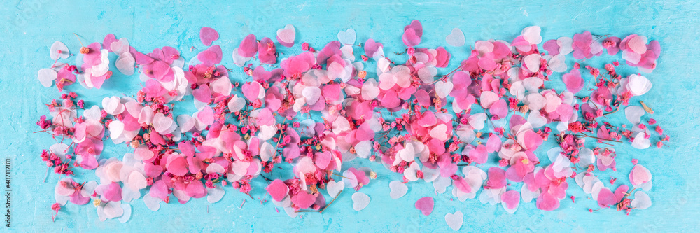 Valentine day panorama with pink hearts and flowers confetti, a flat lay panoramic banner on a blue background