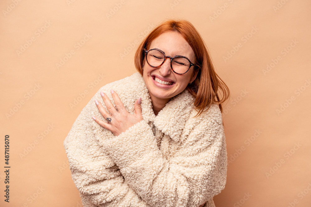 Young caucasian woman isolated on beige background laughing and having fun.