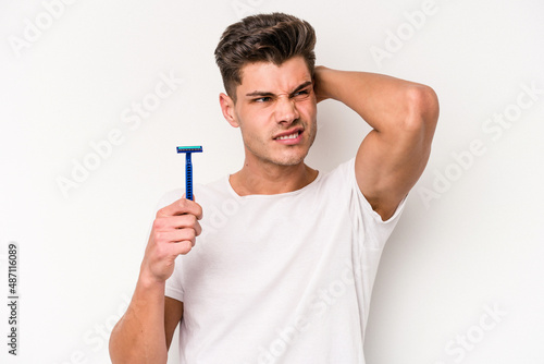 Young caucasian man shaving his beard isolated on white background touching back of head, thinking and making a choice.