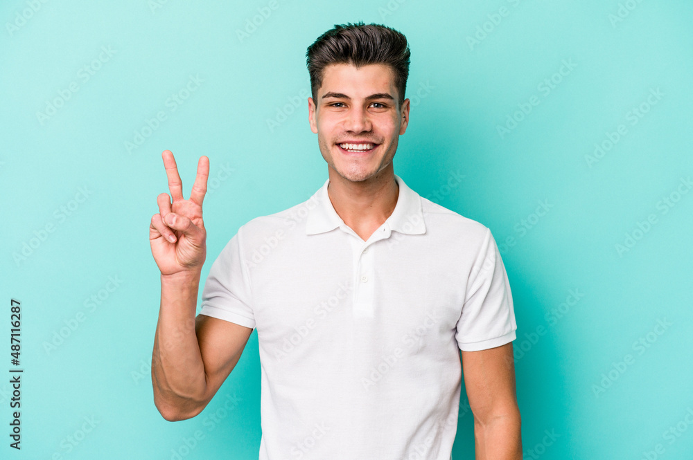 Young caucasian man isolated on blue background showing victory sign and smiling broadly. Young caucasian man isolated on blue background showing victory sign and smiling broadly.